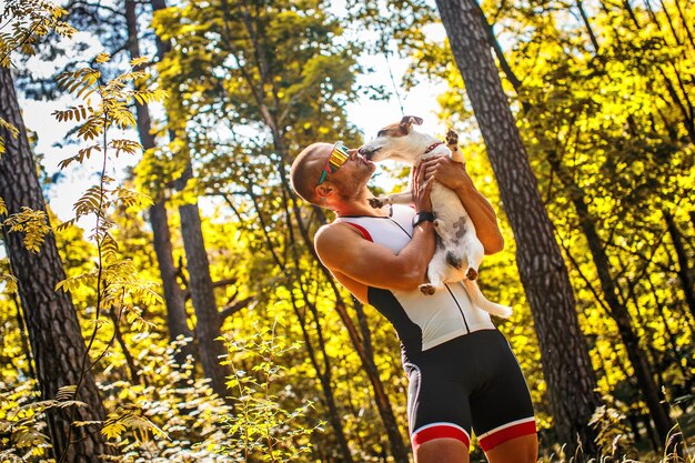 緑の森で彼の小さな犬と一緒にスポーツウェアとサングラスのスポーツマン。