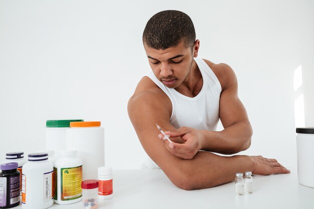 sportsman standing over white wall holding syringle make injection
