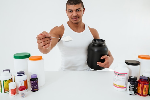 Sportsman standing over white wall holding vitamins