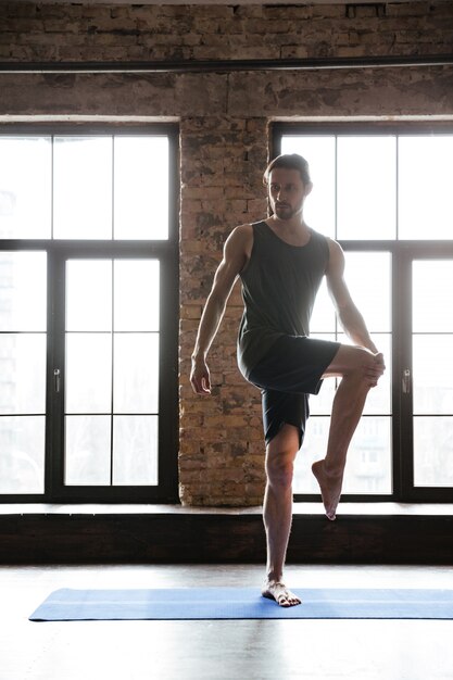 Sportsman stretching leg muscles while standing on the mat