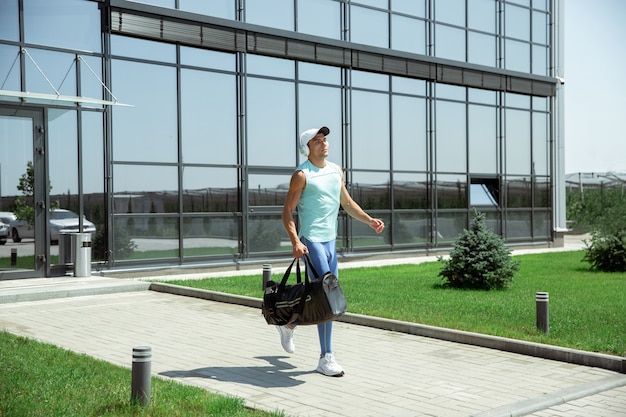 Sportsman walking down against modern glassed building, airport in megapolis in summer's day.