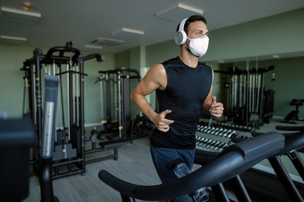 Sportsman with protective face mask running on treadmill in a gym