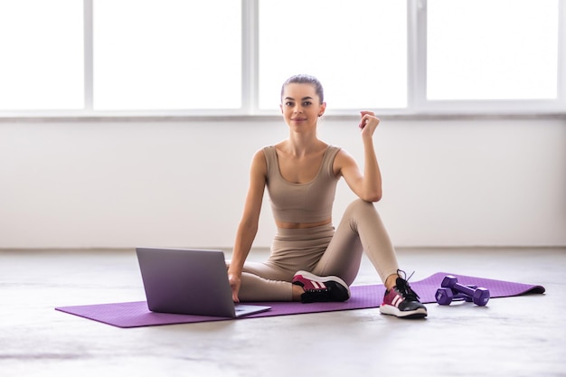 Sportswoman crossing legs while sitting on the mat and doing stretching exercises