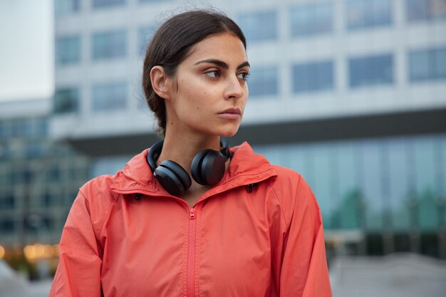 Sportswoman has workout routines looks thoughtfully away thinks about winning competition listens cool soundtracks in headphones going to creat video for her sport blog or conduct online lesson