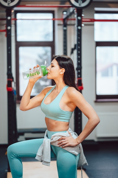 Sportswoman resting and drinking water on stairs in gym