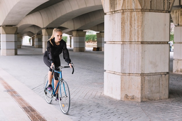 Free photo sportswoman riding bicycle under bridge