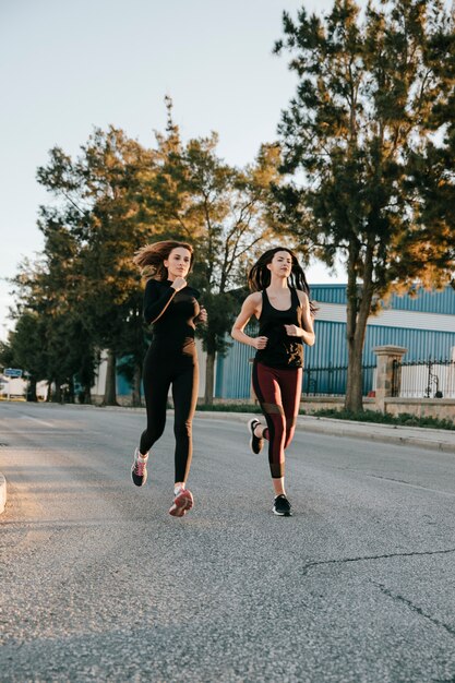 Sportswomen running on street in sunlight