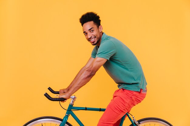 Sporty african man with black hair posing on bicycle. Joyful smiling guy fooling around.