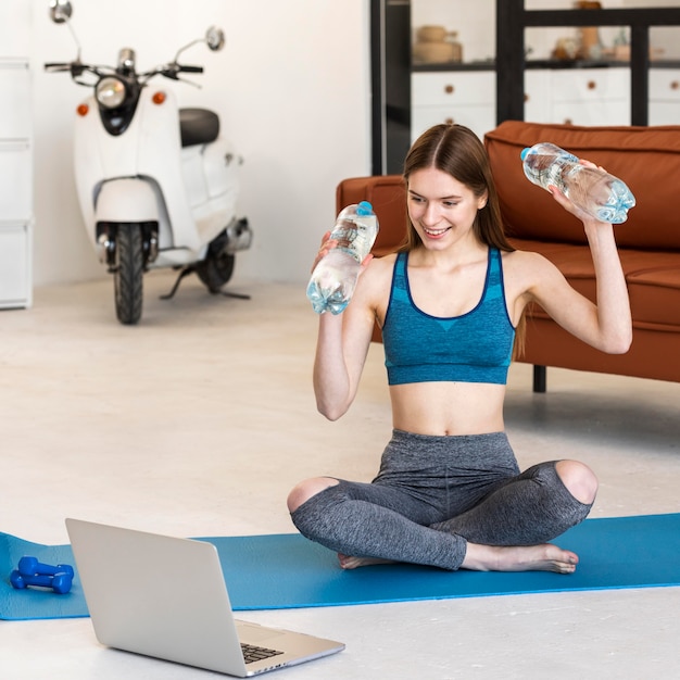 Sporty blogger holding bottles of water in front of laptop