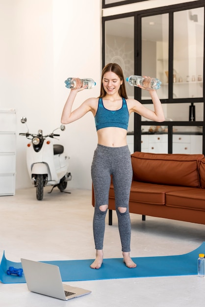 Sporty blogger standing and holding bottles of water in front of laptop