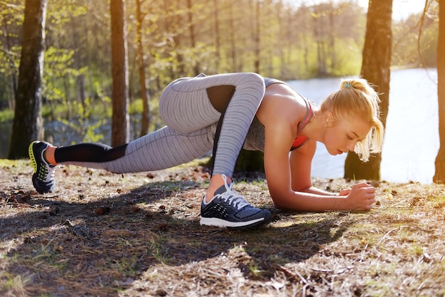 Foto gratuita femmina bionda sportiva che fa esercizi di fitness vicino al fiume selvaggio in una calda giornata estiva.