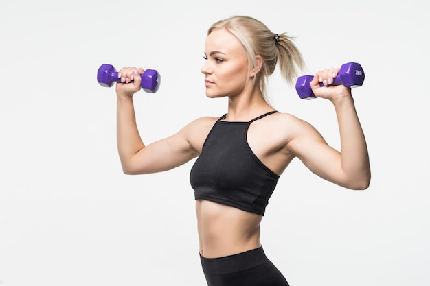 Sporty blonde young girl with fit muscular body works with dumbbells in studio on white