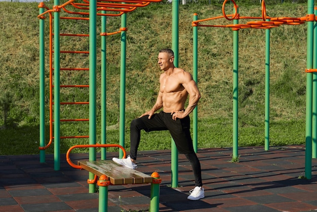 Sporty caucasian man stretching legs on bench outdoors