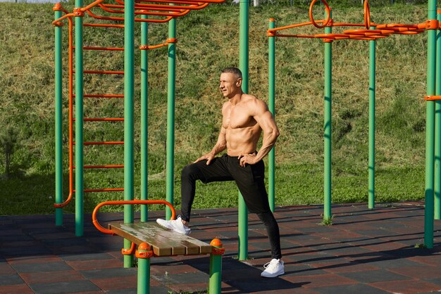 Sporty caucasian man stretching legs on bench outdoors