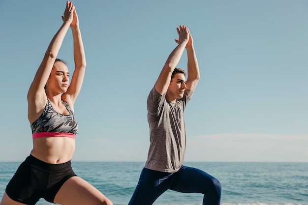 Foto gratuita coppia sportiva facendo yoga in spiaggia