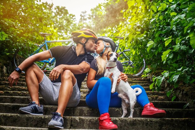 Sporty couple posing with ther dog after bycicle riding in a forest.