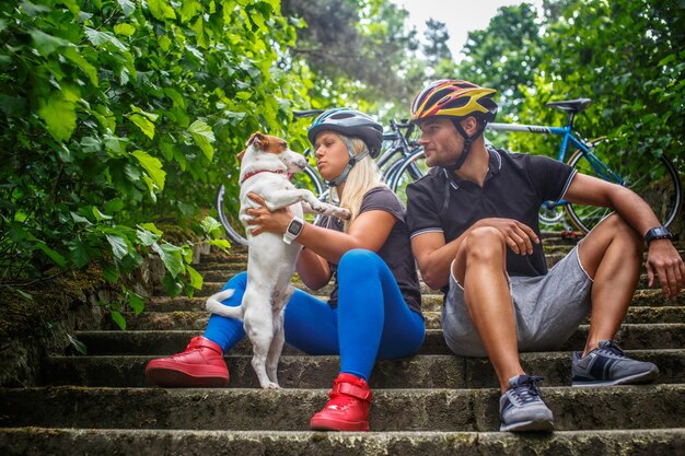 森に自転車に乗った後、犬と一緒にポーズをとるスポーティなカップル。