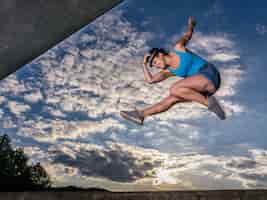 Free photo sporty european female jumping up in the air on cloudy sky background