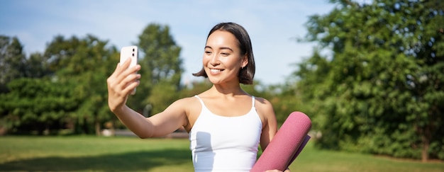 Free Photo sporty fitness girl takes selfie with rubber yoga mat in park does workout and shares photos on