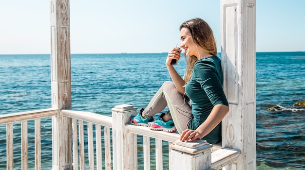 Foto gratuita ragazza sportiva sul molo con il telefono