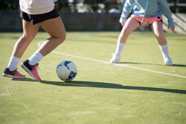 녹색 필드에 축구 공을 전달 하는 스포티 한 여자. 운동복을 입은 두 어린 소녀가 함께 축구를 하고 빠르고 전문적으로 공을 차고 있습니다. 건강한 라이프 스타일과 여자 축구 개념