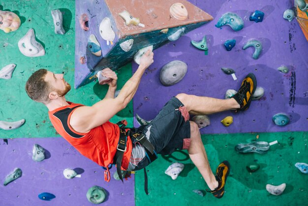 Sporty man climbing wall in gym