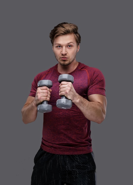 Sporty man in a red t shirt holds dumbbells.