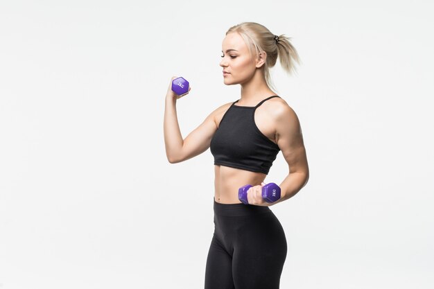 Sporty pretty blonde young girl with fit muscular body works with dumbbells in studio on white