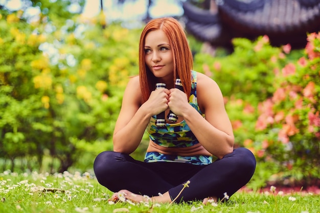 Free photo sporty redhead female relaxing in outdoor summer park.