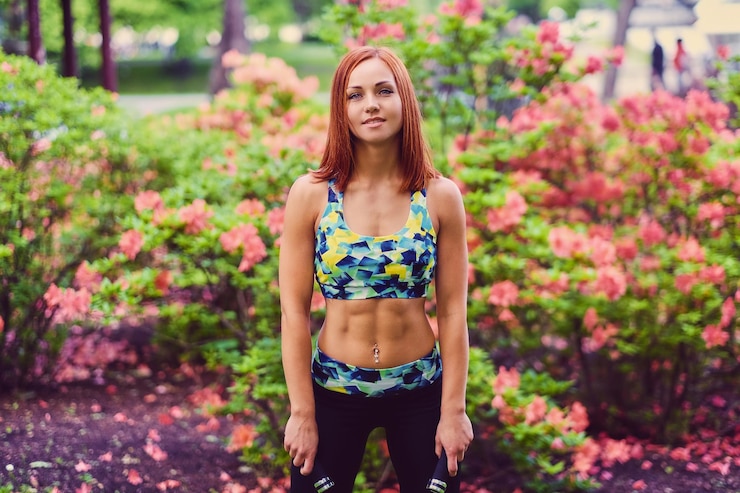Free Photo sporty redhead female relaxing in outdoor summer park.