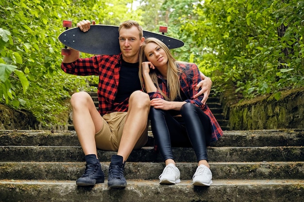 Free photo sporty urban couple relaxing on the steps after longboard ride.