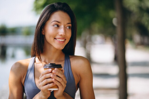 公園の中でコーヒーを飲むスポーティな女性