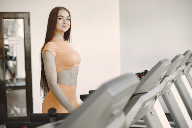 Sporty woman exercising in a gym. She is on a treadmill. Orange active wear.