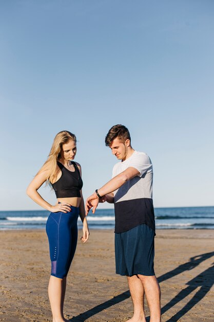 Sporty woman and man looking at watch at the beach