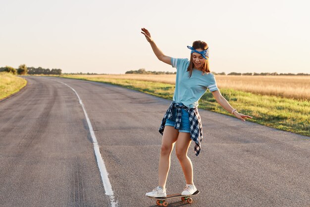 路上でスケートボードに乗るスポーティな女性。ロングボーディングを楽しんだり、手を上げたり、幸せな集中表現、健康的なライフスタイル、コピースペースを楽しんでいるスリムなスポーティな女性。