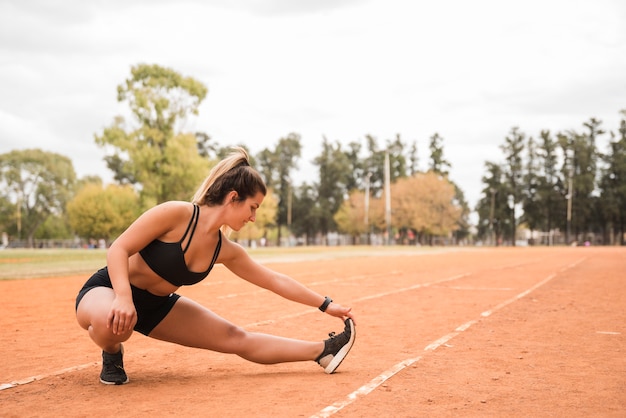 スポーティな女性のスタジアムのトラックでストレッチ