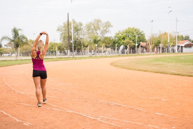 スポーティな女性のスタジアムのトラックでストレッチ