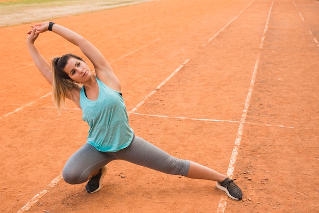 Sporty woman stretching on stadium track