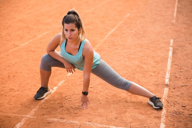 スポーティな女性のスタジアムのトラックでストレッチ