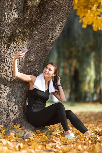 Foto gratuita donna sportiva che prende i selfie vicino ad un albero