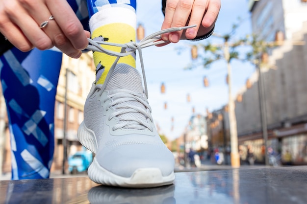 Sporty woman tying shoelace on sneakers before training. Female athlete preparing for jogging outdoors. Runner getting ready for morning running routine. Sport active lifestyle concept. Close-up