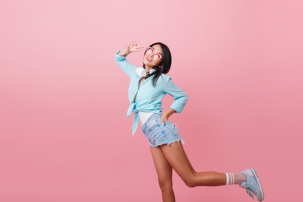 Sporty woman with bronze skin funny dancing with positive face expression. graceful latin girl in blue attire posing on one leg.