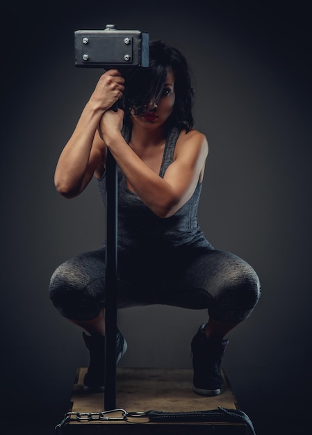 Sporty woman with short black hair sitting on wooden box and holding big black hummer.