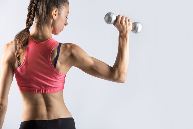 Sporty woman working out with weights. Rear view