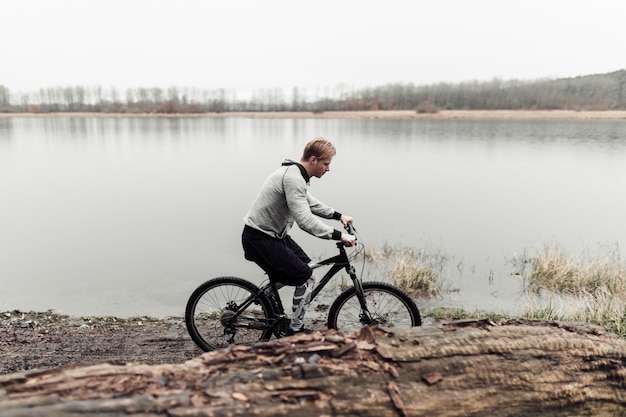 Free photo sporty young man riding bicycle near the lake