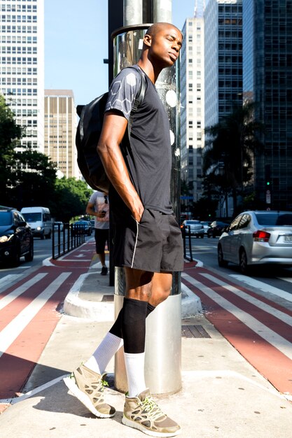 Sporty young man with backpack leaning on road with hands in the pocket