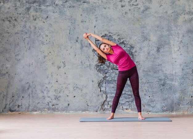 Sporty young woman doing fitness exercise standing against grey wall