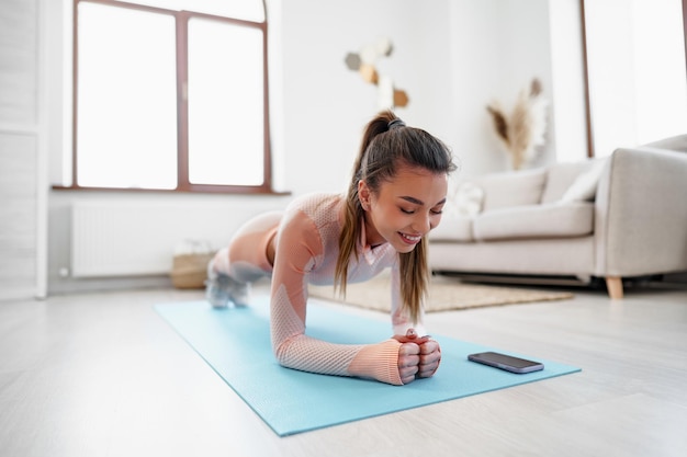 Спортивная молодая женщина делает упражнения на доске в помещении дома