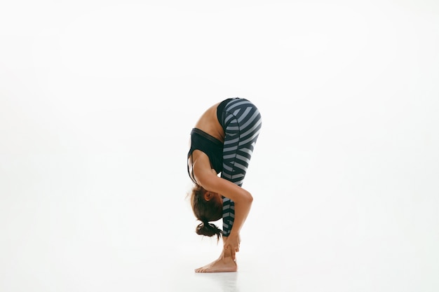 Спортивная молодая женщина делает практику йоги изолированной на белой стене. Подходит гибкая женская модель, практикующая. Концепция здорового образа жизни и естественного баланса между телом и умственным развитием.
