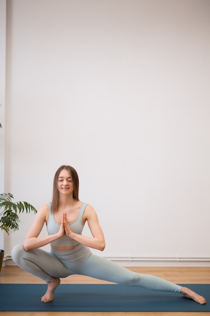 Sporty young woman doing yoga practice on white wall with plants - concept of healthy life and natural balance between body and mental development